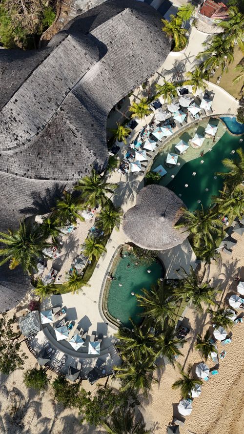 Free Stunning aerial shot of a tropical beach resort with pools, palm trees, and thatched roofs. Stock Photo