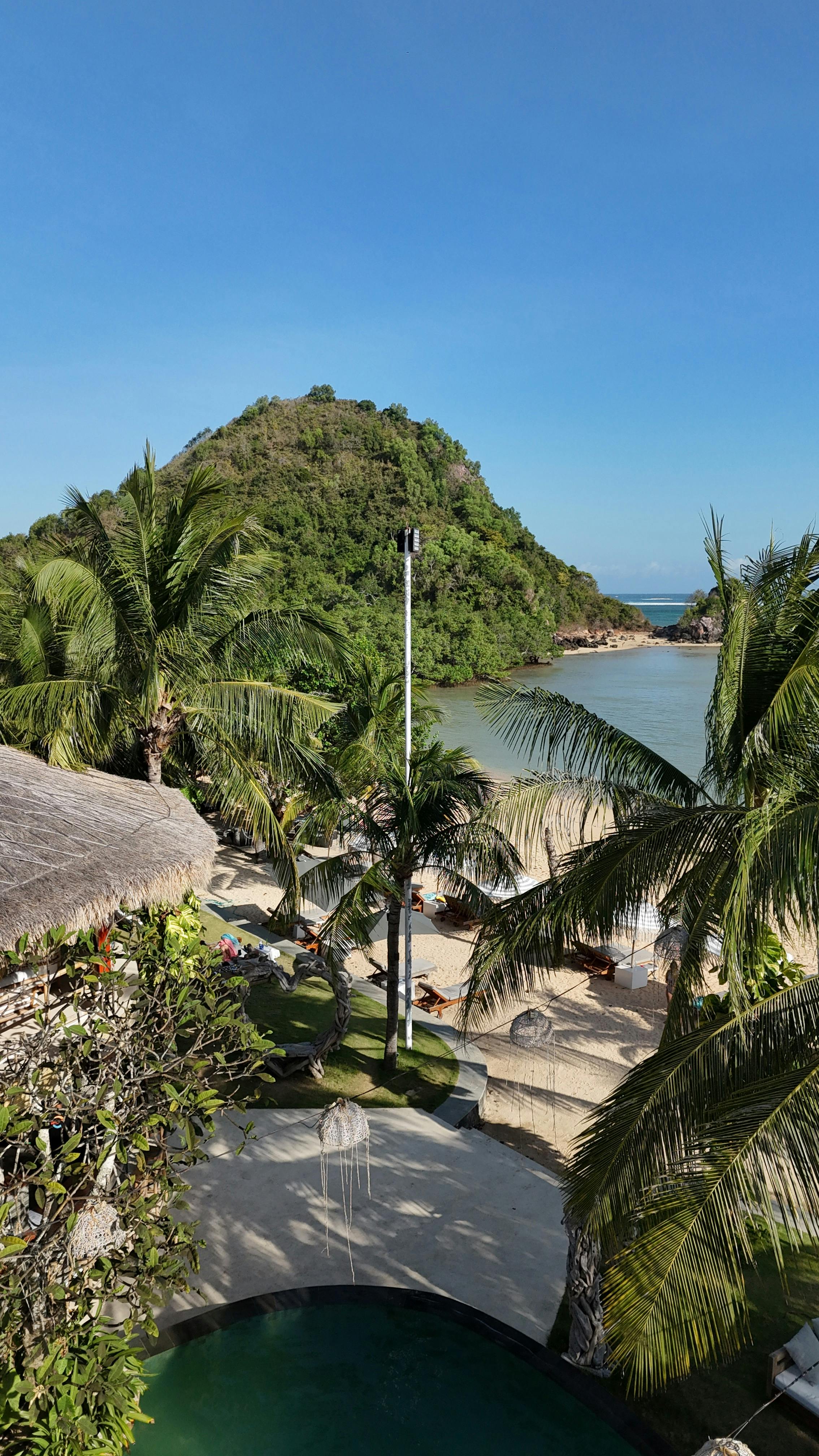Gratis Vista panoramica di un resort tropicale sulla spiaggia, con colline lussureggianti e palme sotto un cielo azzurro e terso. Foto a disposizione