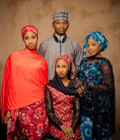 Free Four young adults in traditional attire pose in a warm-toned studio setting. Stock Photo