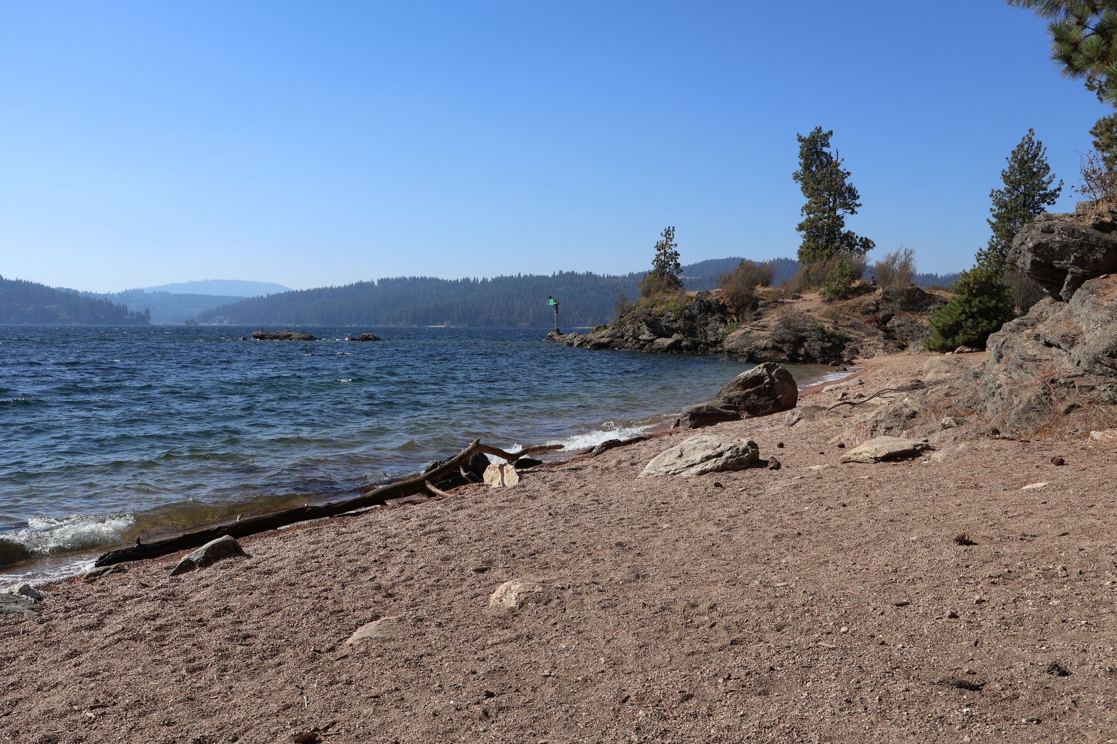 Tranquil beach view of Coeur d'Alene Lake with scenic mountains and clear skies in Idaho.