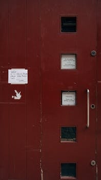 Red door with small windows and posted notices outdoors.