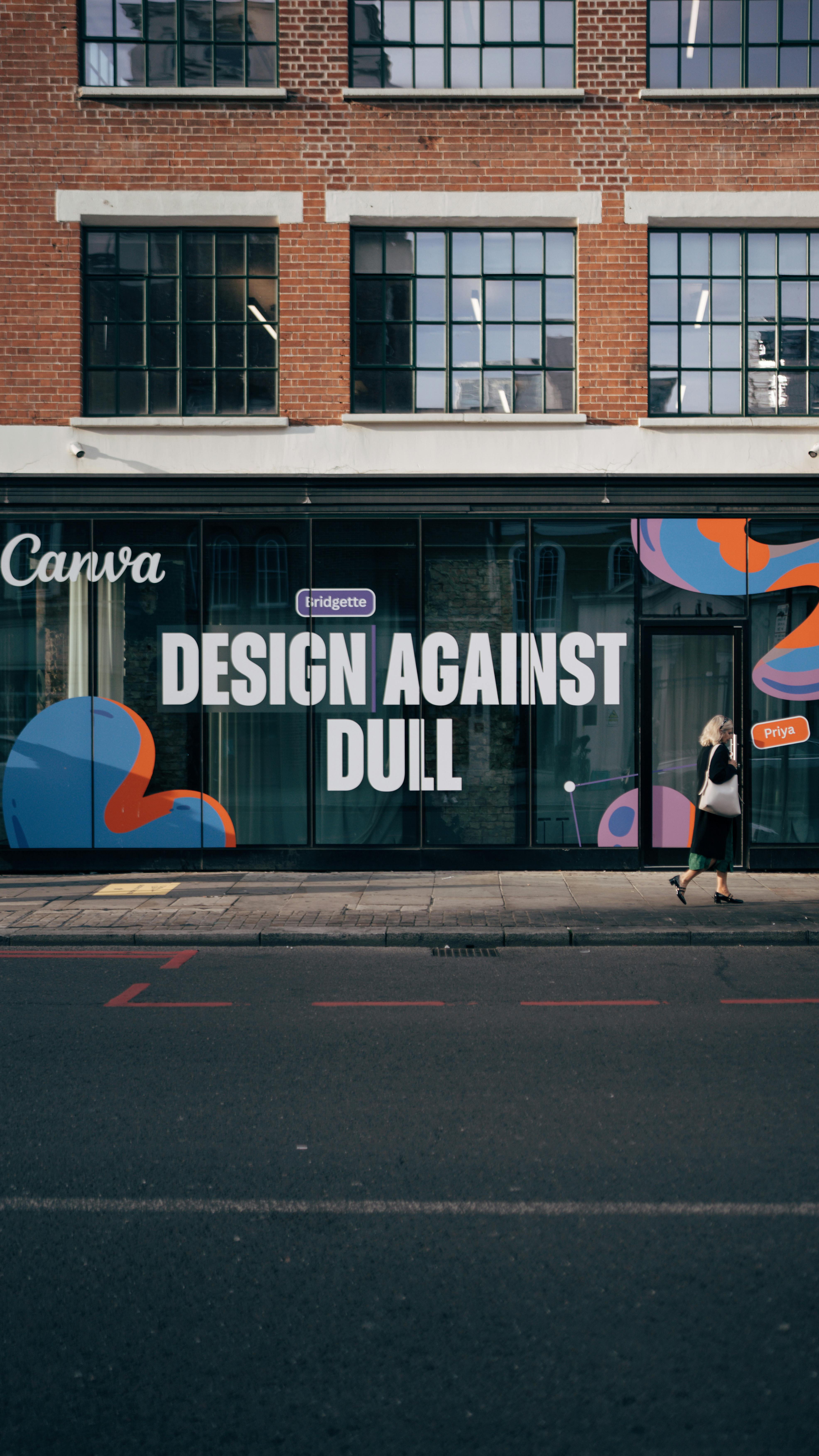 Street mural with 'Design Against Dull' slogan on a modern urban building facade.