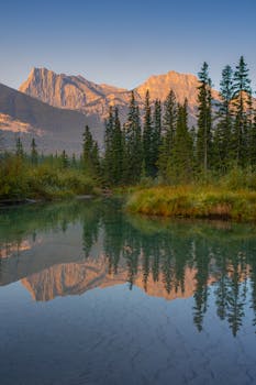 Peaceful dawn scene of Canmore mountains mirrored in calm water, showcasing stunning natural beauty.