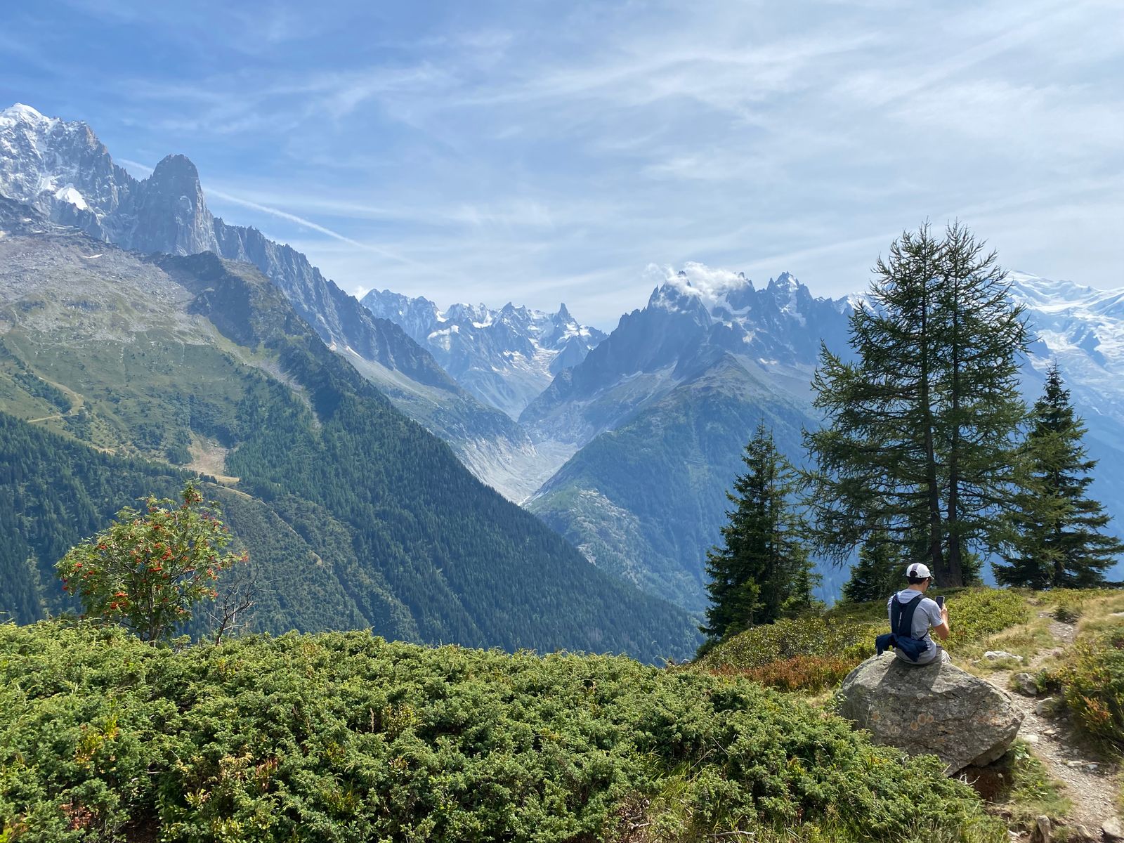 Trekker on a green alpine trail with the glaciated Mont Blanc range rising behind, Chamonix valley