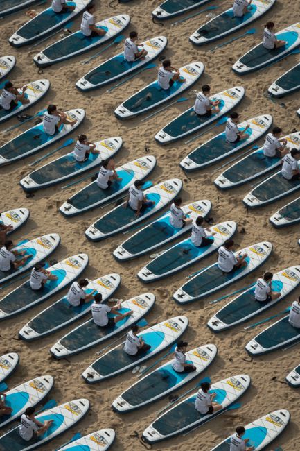 Aerial shot of people on surfboards lined up on a sandy beach in Busan, South Korea.