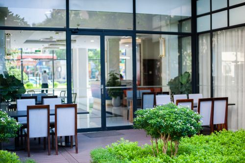 Free Contemporary outdoor dining area with glass wall, seating, and lush greenery. Stock Photo