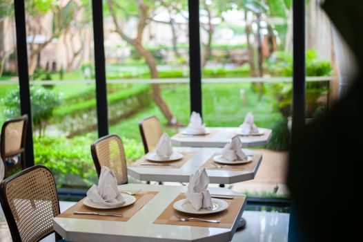 Beautifully set dining tables in an elegant restaurant overlooking a lush green garden.