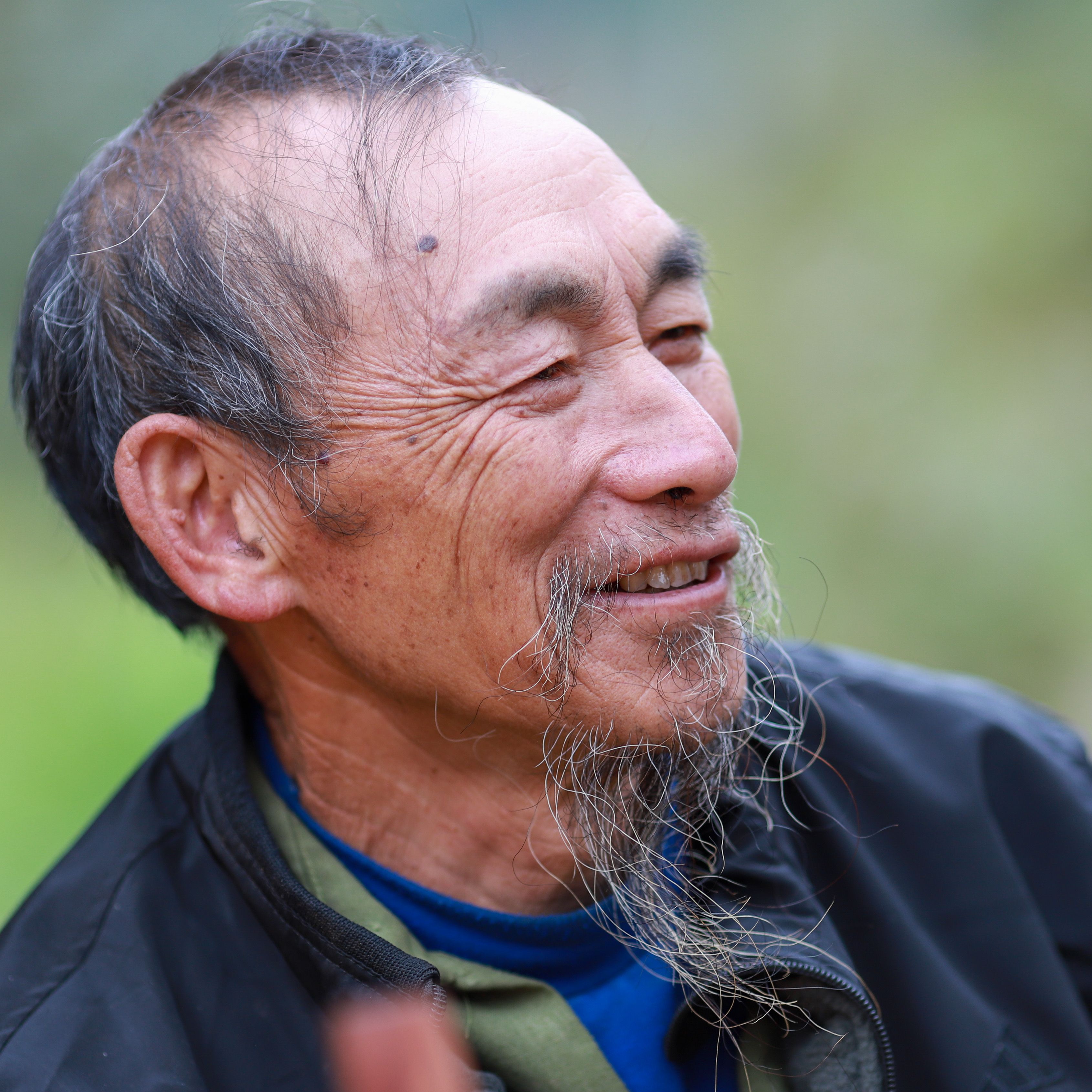 Portrait of a smiling elderly Hmong man outdoors in Lào Cai, Vietnam, capturing cultural identity and happiness.