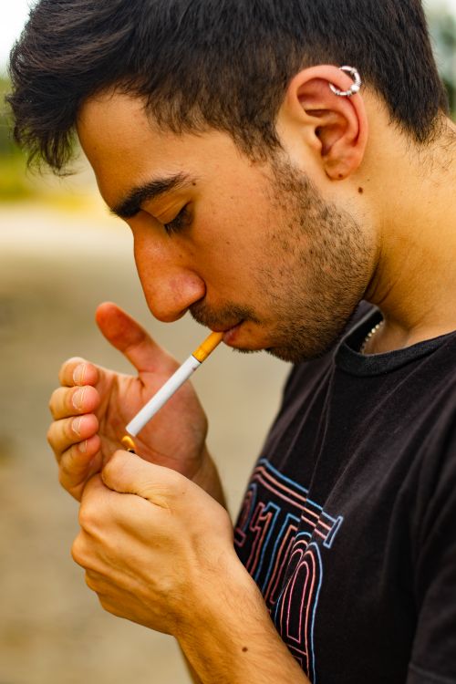Free Close-up of a young man lighting a cigarette outdoors in Linares. Stock Photo