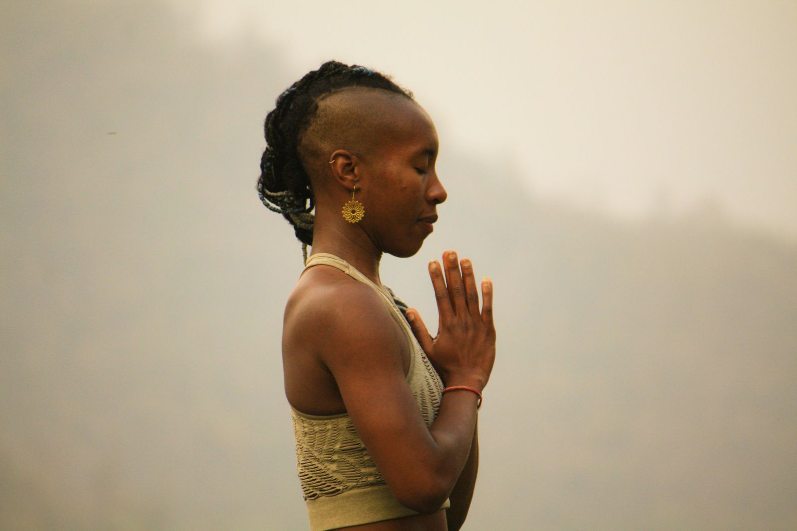 Woman standing outdoors in pranamasana prayer pose with palms pressed together at the chest