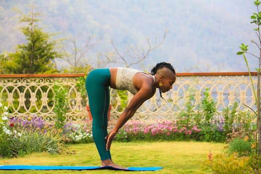 A woman practices yoga outdoors in Rishikesh, India, surrounded by a lush garden and scenic mountain views.