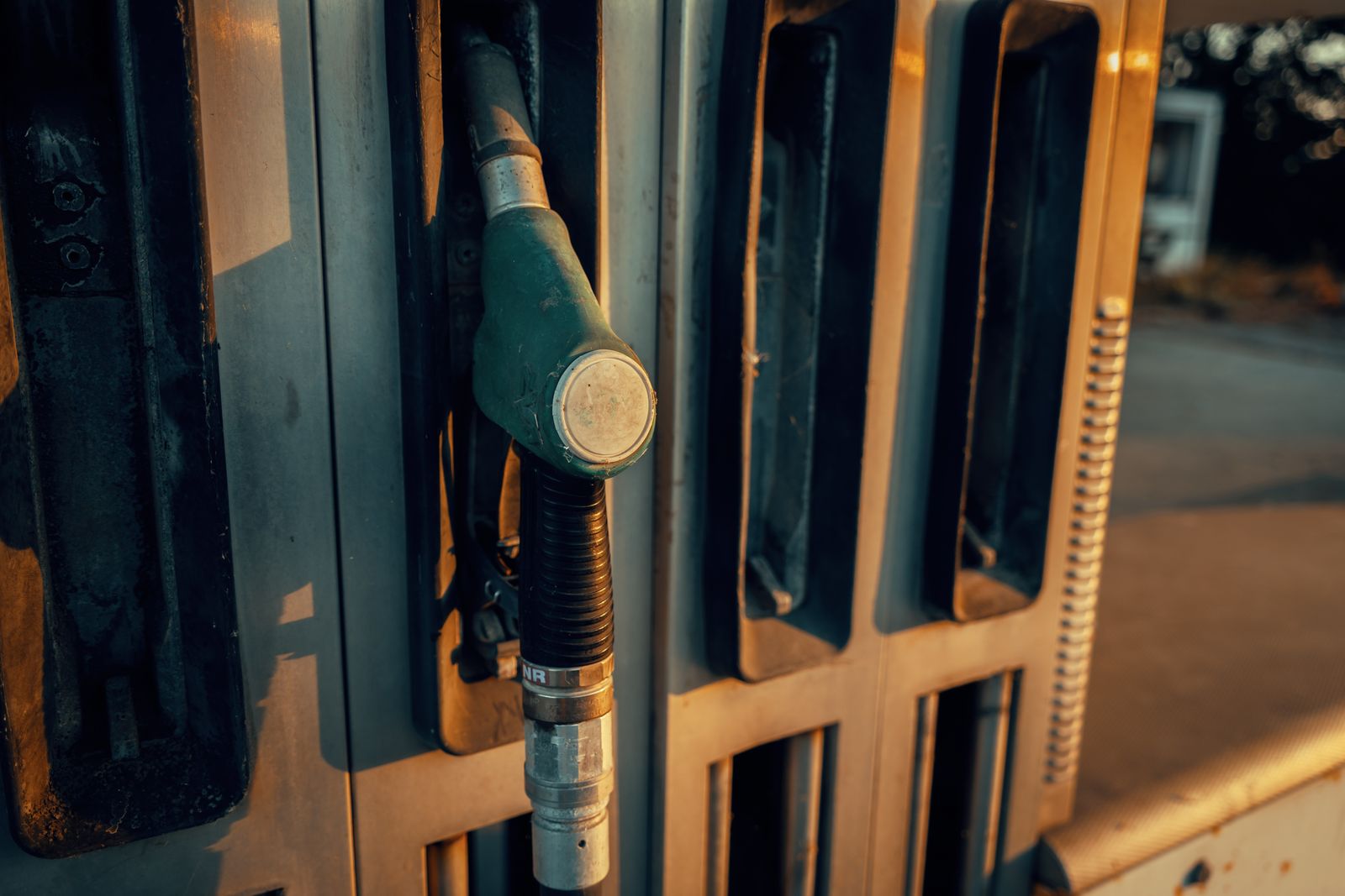 Fuel nozzle and hose seated in a dispenser at a retail outlet in late afternoon light.