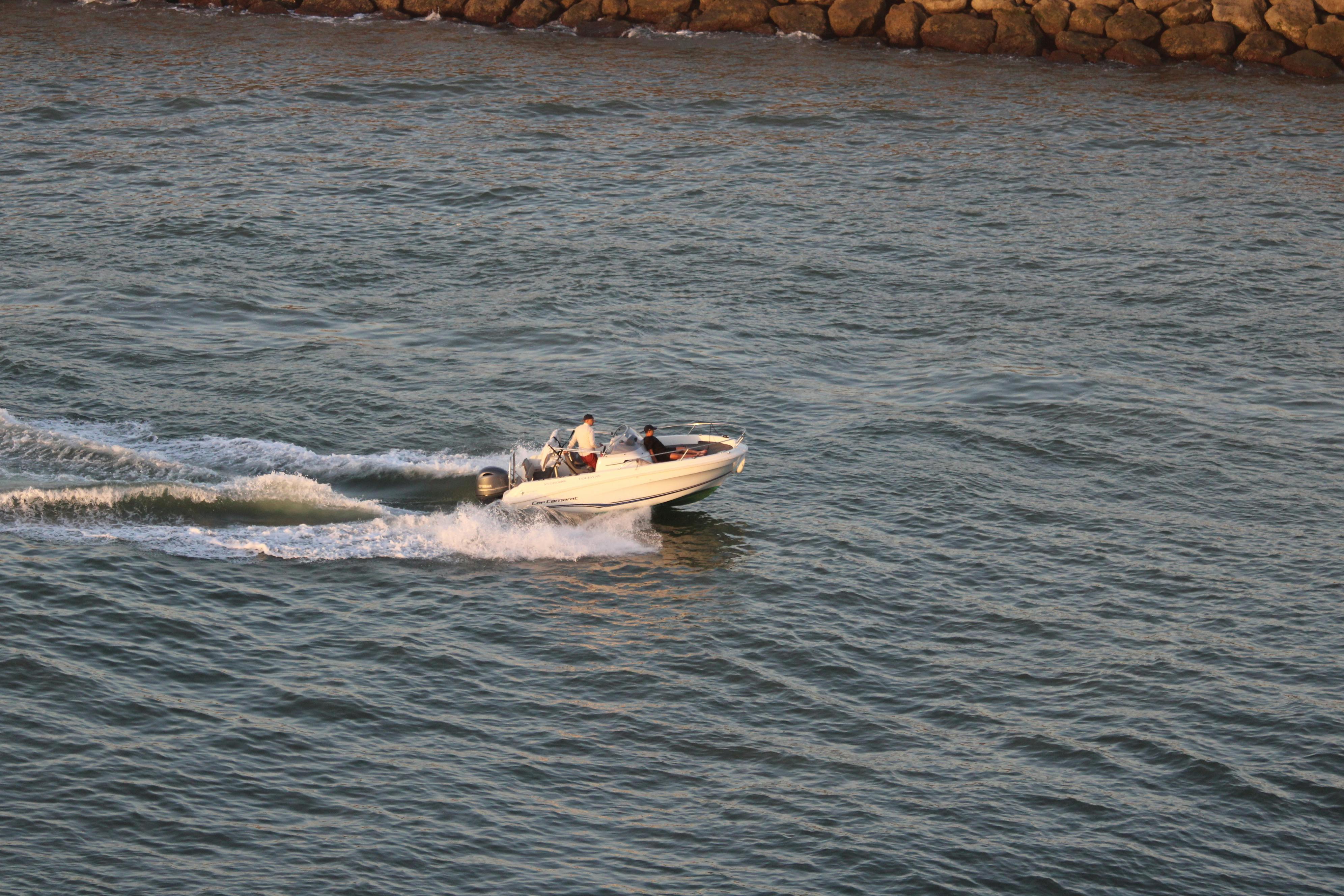 Motorboat speeding along the coastline near a rocky shore, exhibiting dynamic movement on the water.