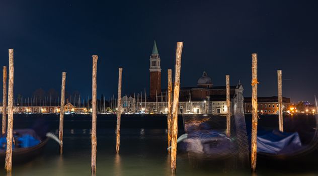 Night view of Venice's San Giorgio Maggiore with blurred gondolas in the foreground.