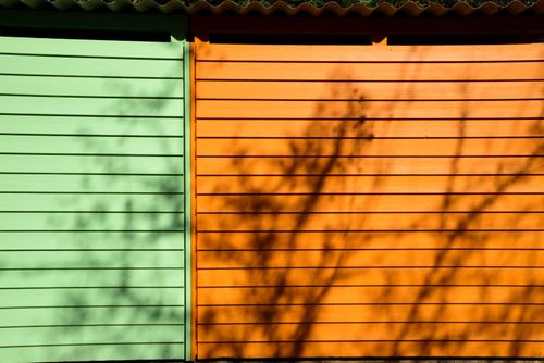 Free Green and orange wooden wall with tree shadows creating a striking visual effect. Stock Photo