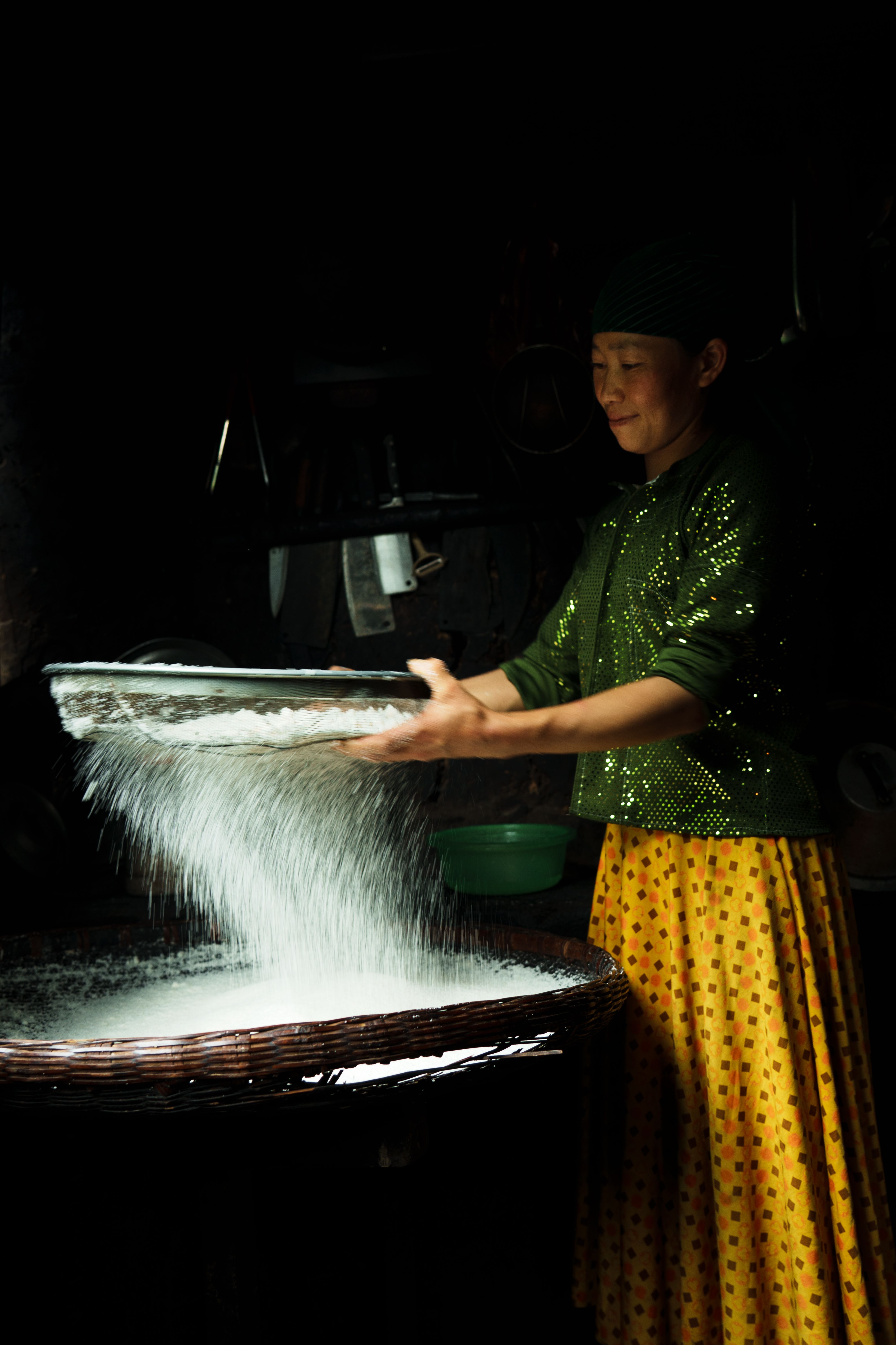 A bowl of fine white rice flour next to a scoop of uncooked white rice grains on a wooden counter