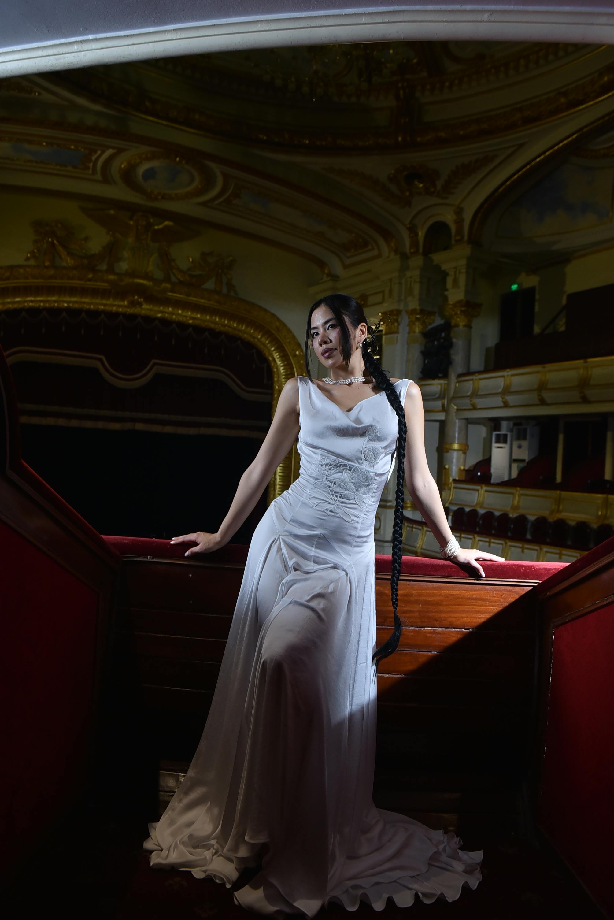 bezplatná Sofistikovaná žena pózuje v bílých šatech na opulentním balkonu divadla. Základová fotografie