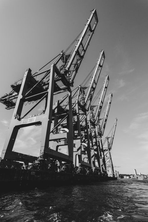 Free Dramatic black and white photo of port cranes by the sea, creating a moody industrial scene. Stock Photo