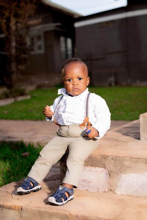Free Charming toddler sitting on steps outdoors, dressed smartly in suspenders, exuding cuteness. Stock Photo