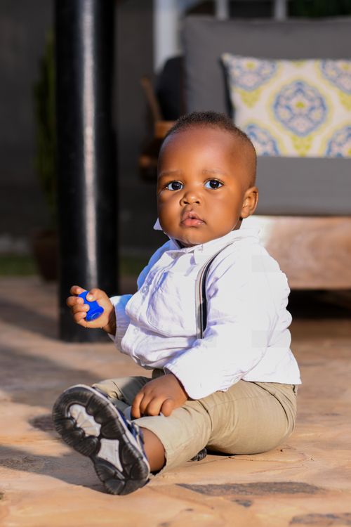 Free Cute baby boy sitting on the patio with a toy, wearing khaki pants and white shirt. Stock Photo