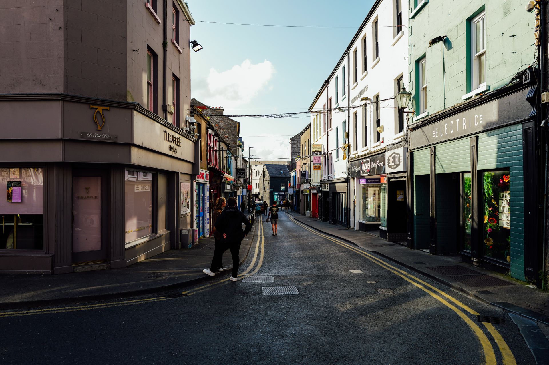 A bustling urban street with shops and people, captured during the day with vibrant lighting.