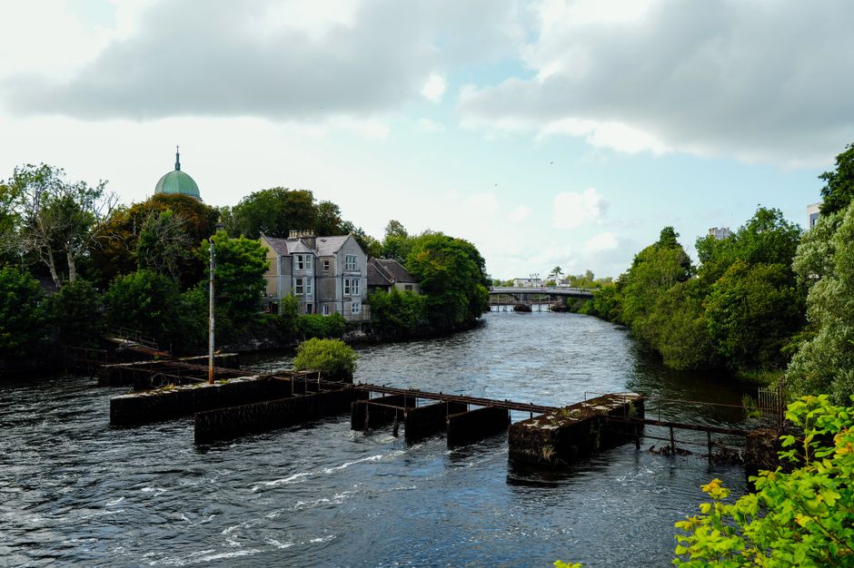 Scenic view of riverside houses and a bridge amidst lush greenery under a cloudy sky. Scenic view of riverside houses and a bridge amidst lush greenery under a cloudy sky.
