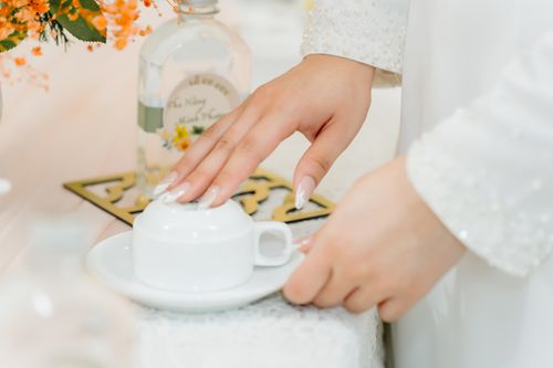 Free Woman's hand gracefully touching an ornate teacup in a serene setting, adorned with floral elements. Stock Photo