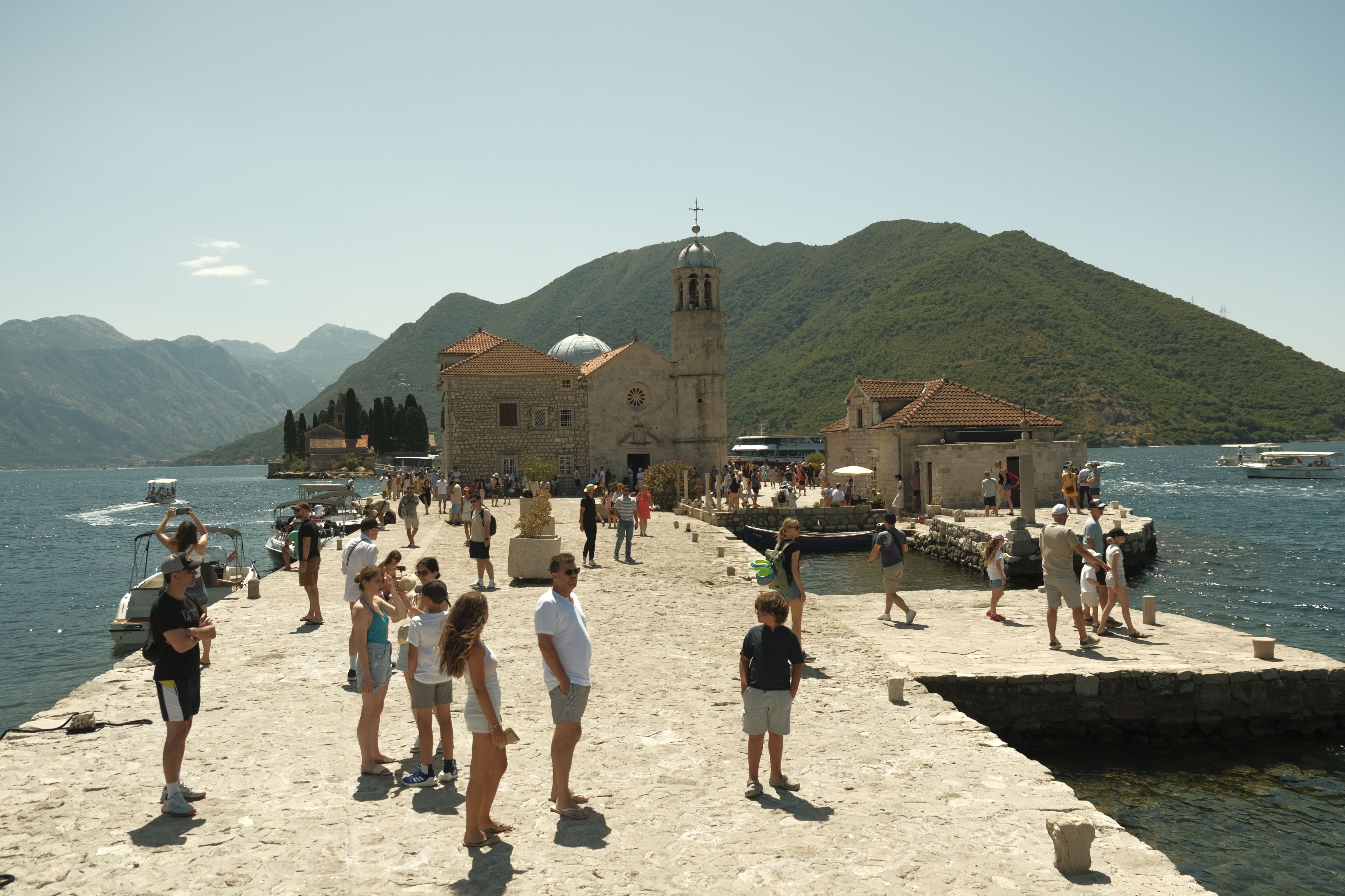 Tourists exploring Our Lady of the Rocks in Perast, Montenegro on a sunny day by the sea. Tourists exploring Our Lady of the Rocks in Perast, Montenegro on a sunny day by the sea.