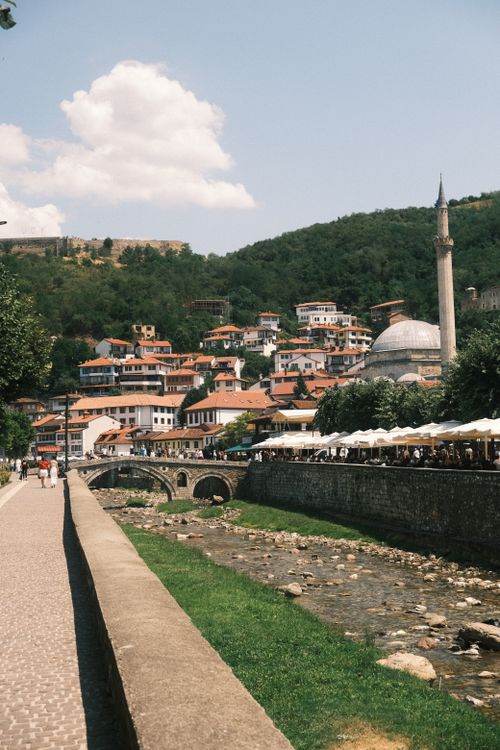 Free Picturesque image of Prizren showcasing a stone bridge, mosque, and hillside with houses under a clear sky. Stock Photo