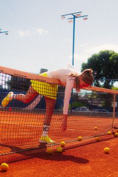 Fun moment captured of a young woman playfully climbing over a tennis net on a bright outdoor court.