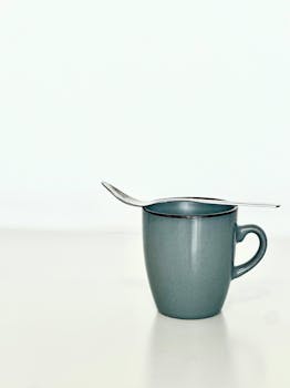 Minimalist photo of a blue ceramic mug with a spoon balanced on top, against a white background.