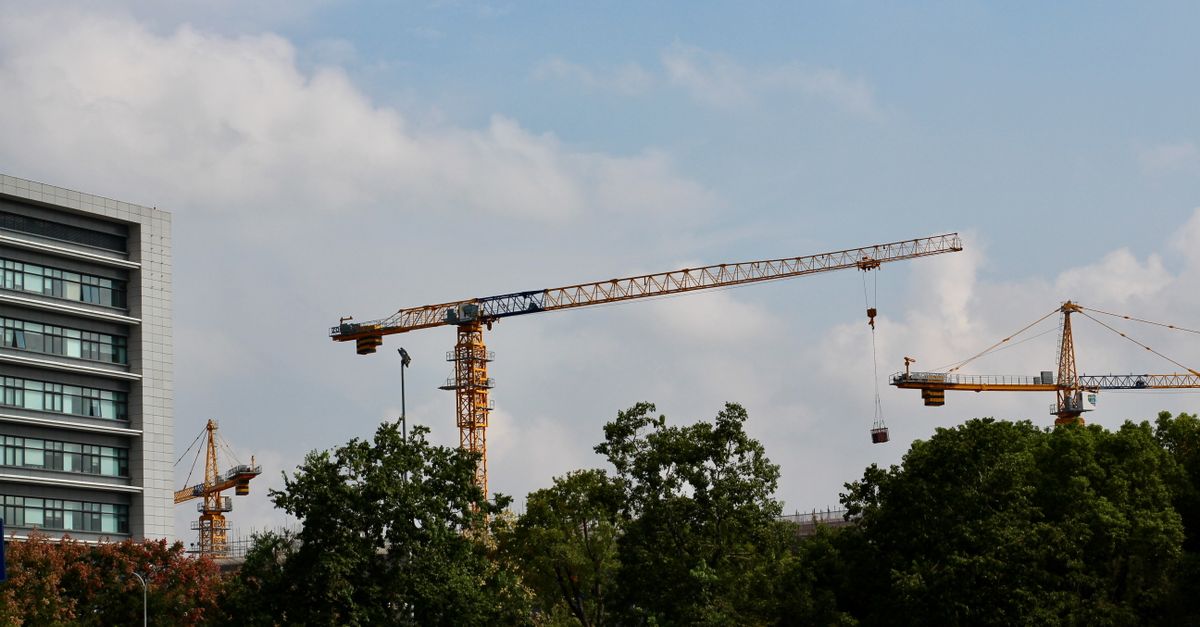 Cityscape featuring multiple tower cranes and a modern building under a clear blue sky.