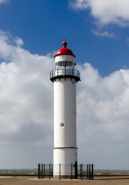 Lighthouse stands tall against the blue sky and clouds in a coastal location