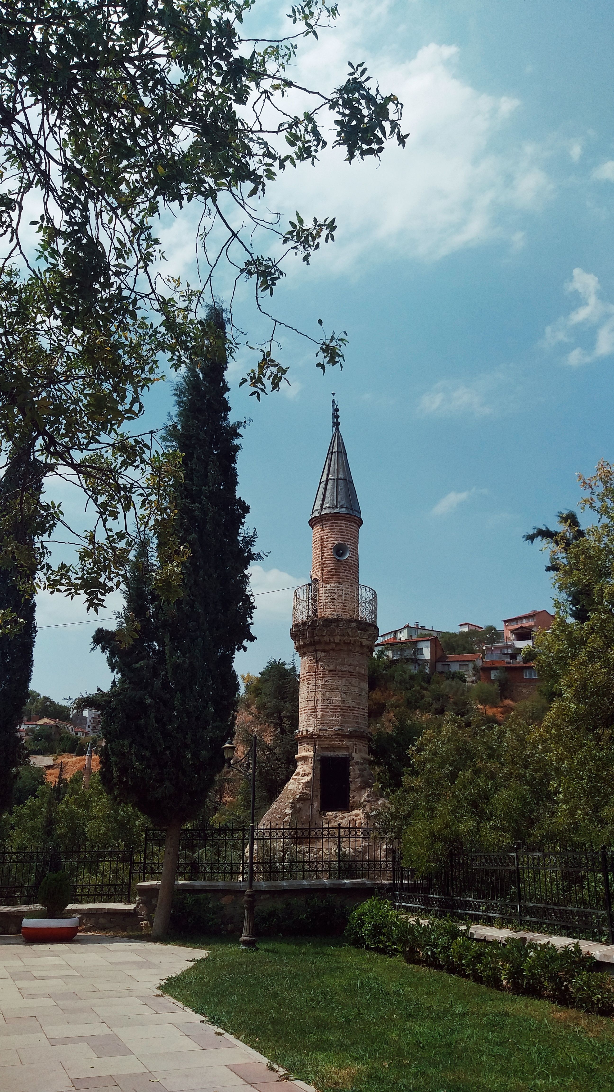 Charming stone clock tower surrounded by lush greenery under a clear blue sky in Bilecik, Türkiye.