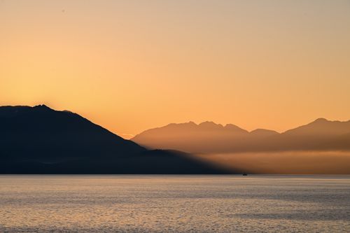 Free A tranquil dawn in Alaska with mountains silhouetted against an orange sky over calm sea waters. Stock Photo