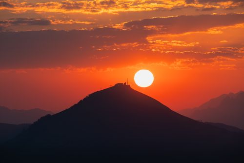 Free A breathtaking sunset over a silhouetted mountain with vibrant orange and red hues. Stock Photo
