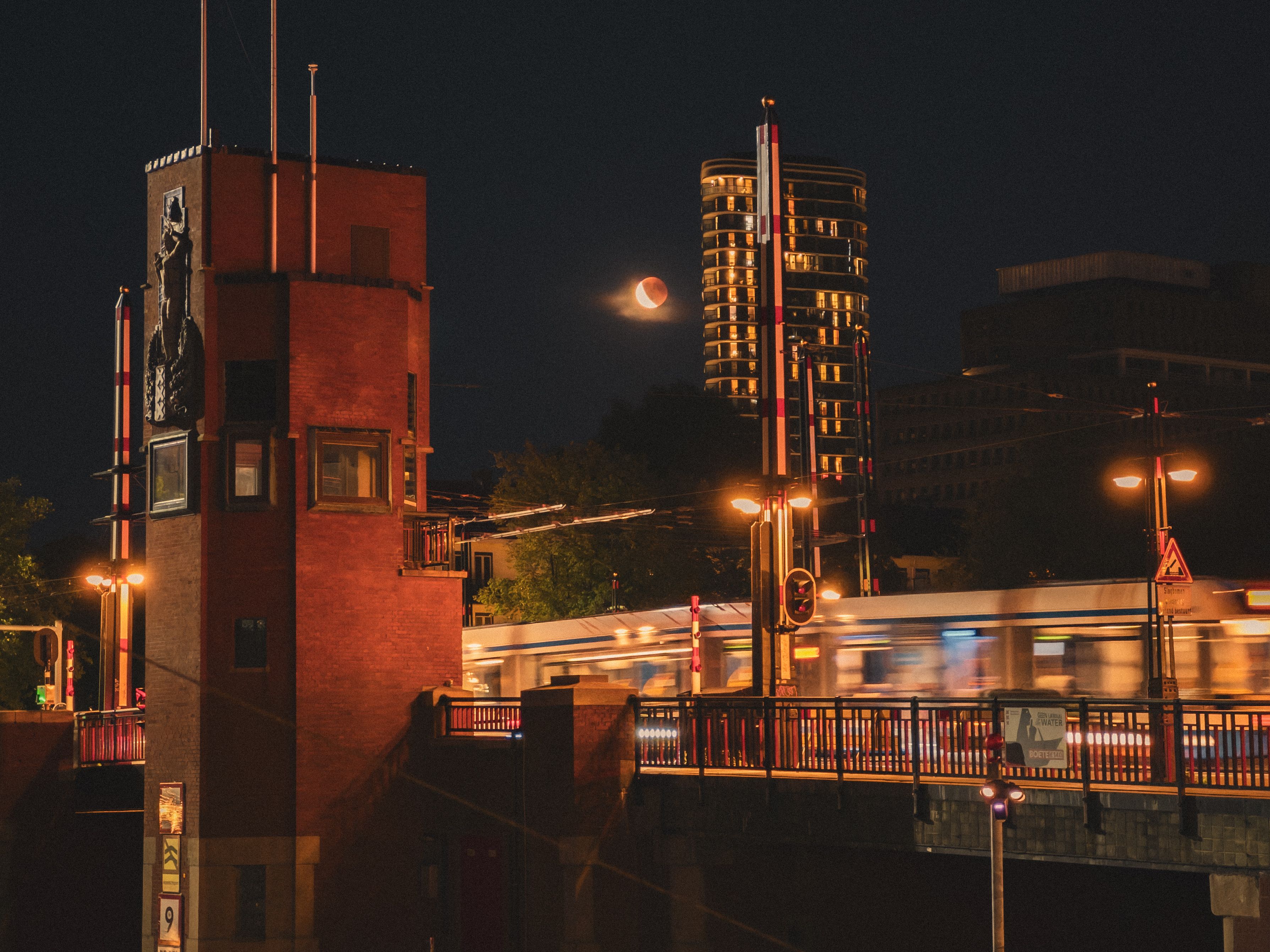 Night view of a tram crossing Magere Brug in Amsterdam with a lunar eclipse visible overhead. - La Haya