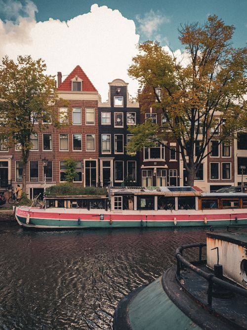 Free Beautiful scene of Amsterdam canal with classic Dutch architecture and houseboats, perfect for travel inspiration. Stock Photo