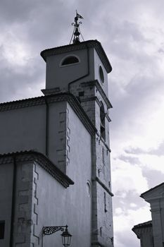 A striking black and white image of a church tower in L'Aquila, Italy, under a dramatic cloudy sky.