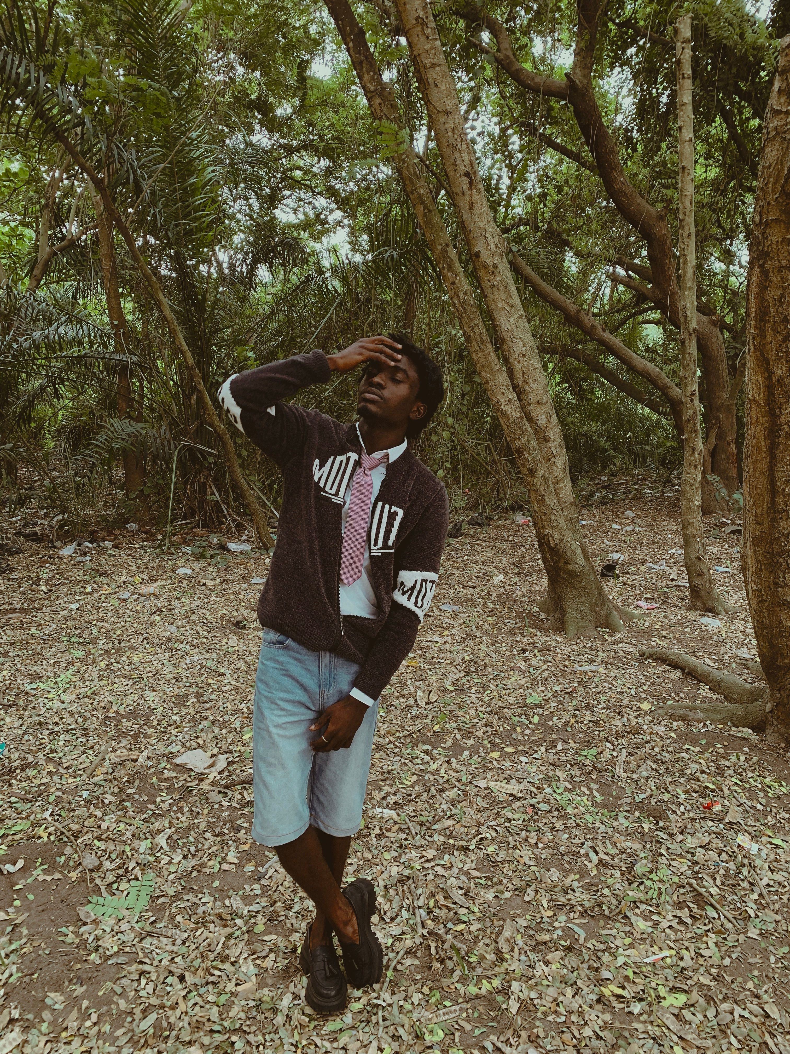 Fashionable man in casual attire posing thoughtfully in a lush forest setting.