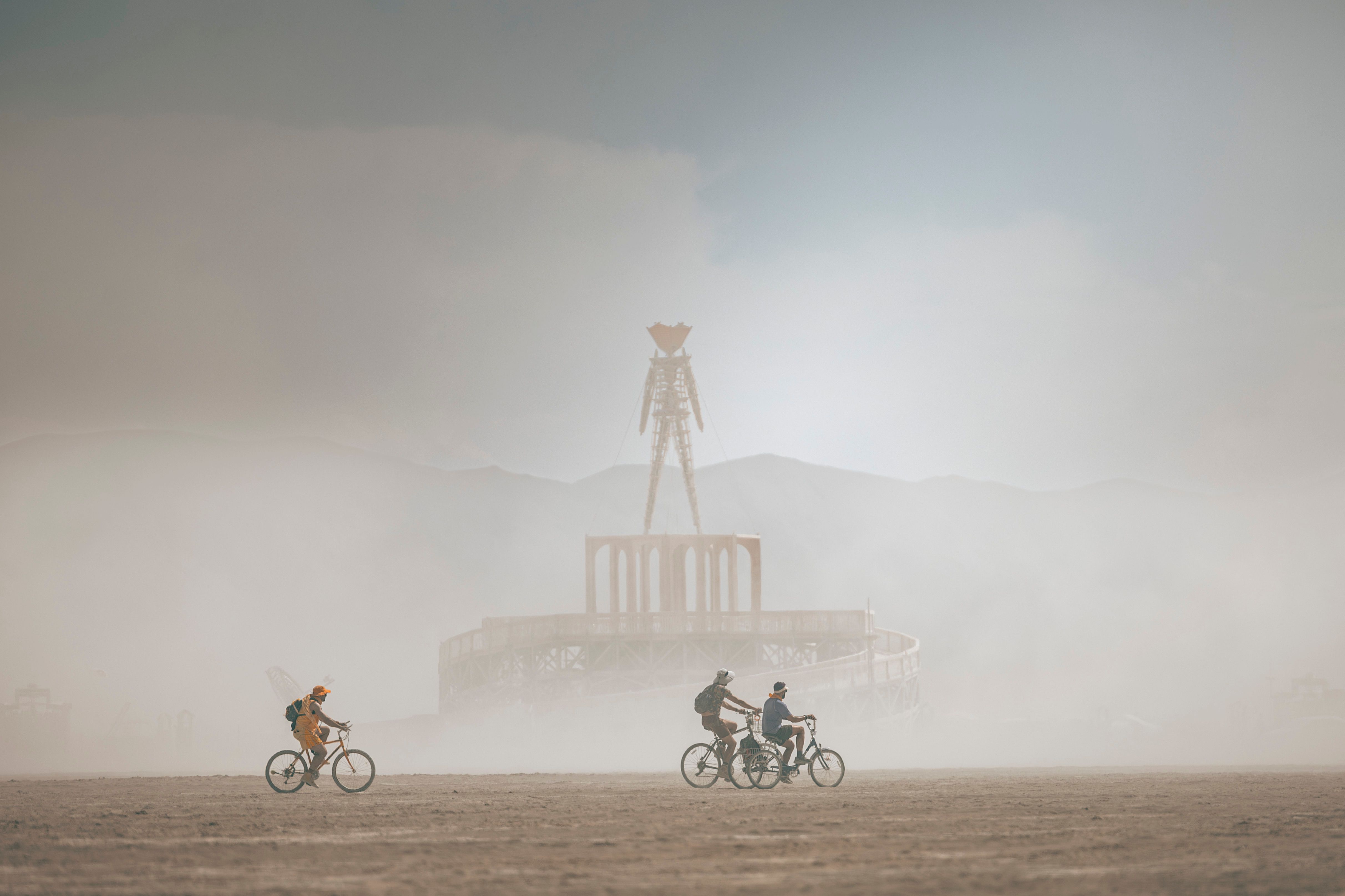 Three cyclists ride through dust at Burning Man festival near the iconic effigy.