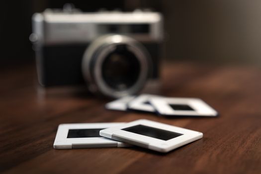 Close-up of vintage camera and slide films on a wooden table, evoking nostalgia.