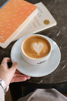 A cappuccino with latte art and books on a marble table, creating a cozy café atmosphere.
