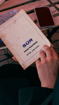 Close-up of a person reading the book "Sür" by Sezai Karakoç in an outdoor café. — photo by güney kayra acer
