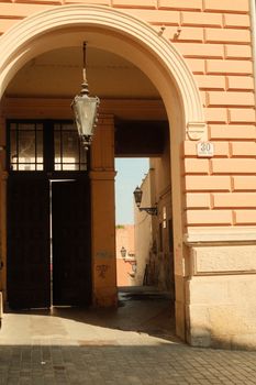 Sunlit historic archway in Zagreb with lanterns casting warm shadows.