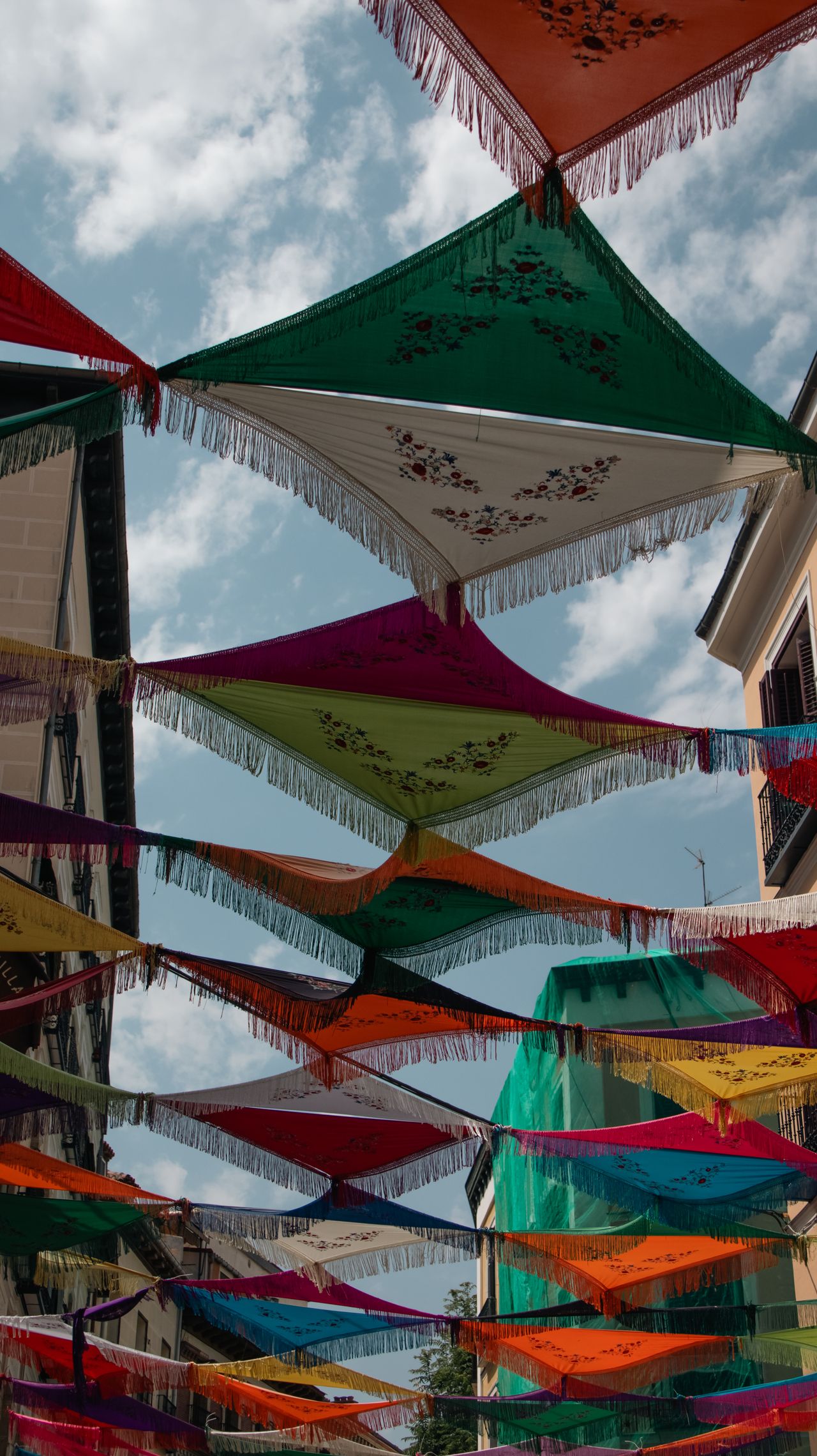 Vibrant fabric canopies adorn a Madrid street, capturing the festive spirit under a bright sky.