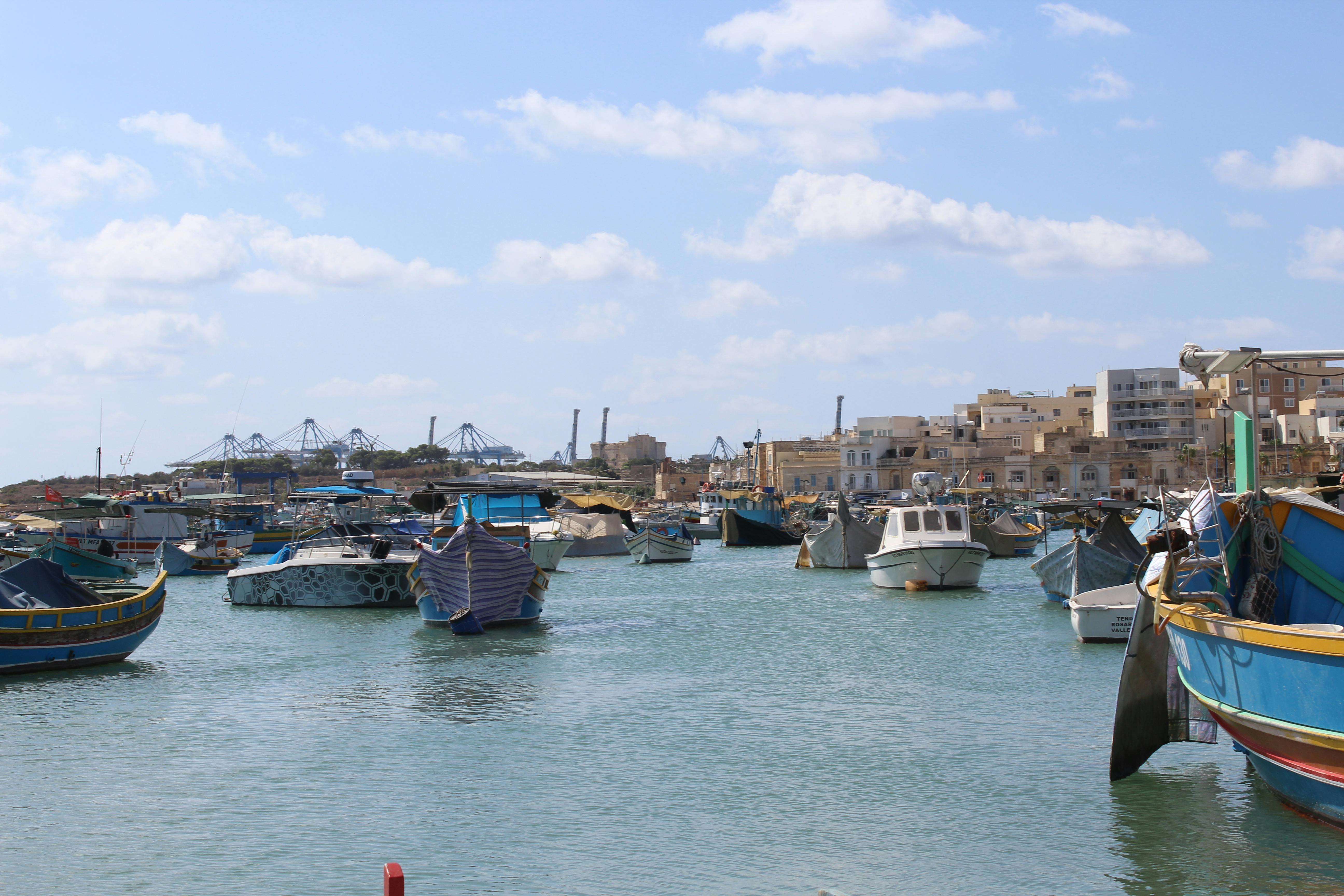 Colorful fishing boats floating in the serene Marsaxlokk harbour under a bright sky.