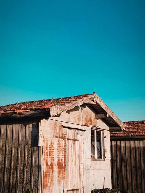Free An old wooden shed with a weathered look stands under a clear blue sky, showcasing rustic charm. Stock Photo