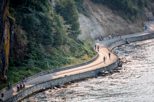 Aerial view of people enjoying the scenic seawall path along Vancouver's coastline under clear skies.