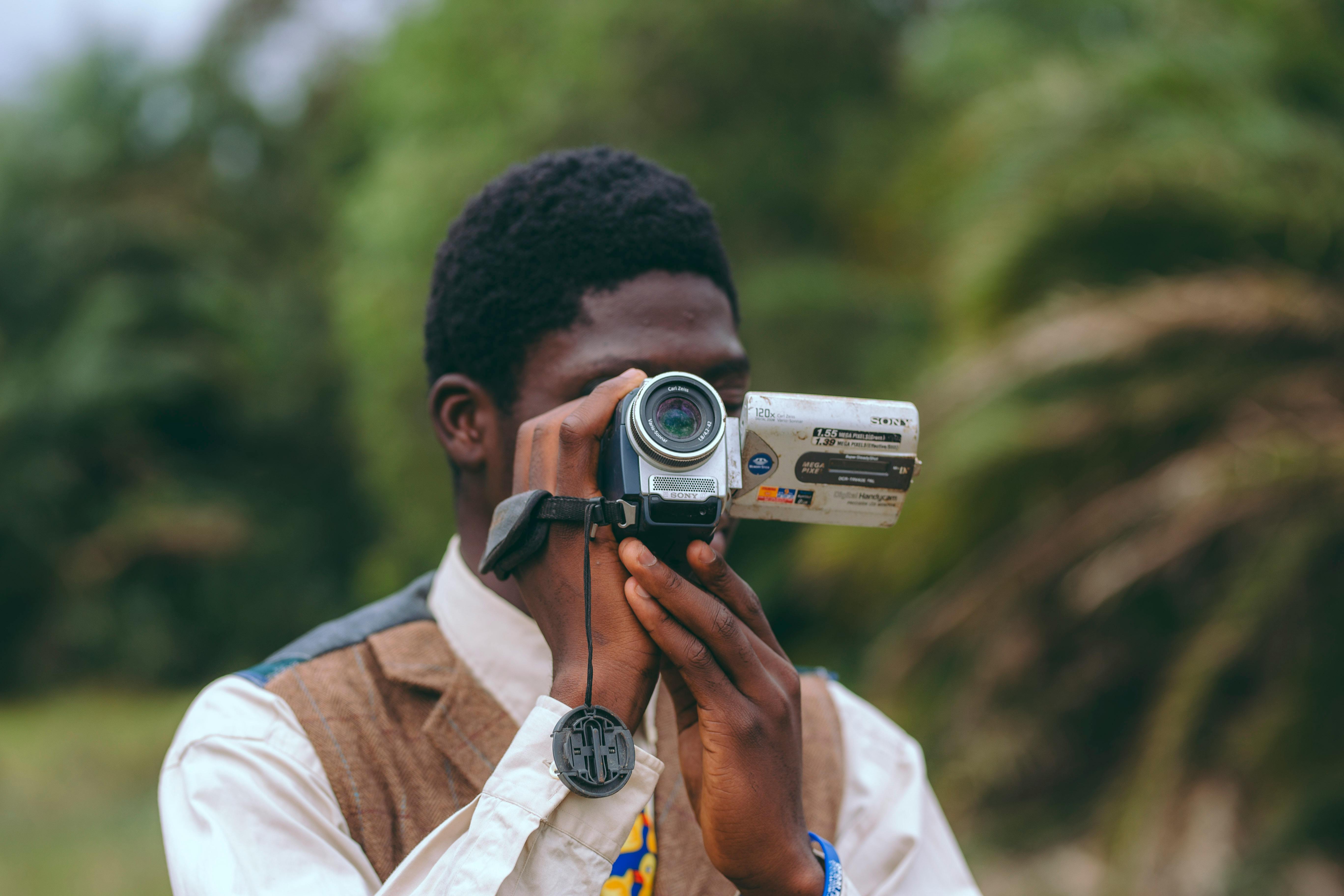 A stylish portrait of a man using a vintage camera in Accra, Ghana's lush outdoors.